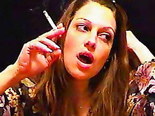 The brunette with a lit cigarette in her hand smokes sexy style and blows it at you.